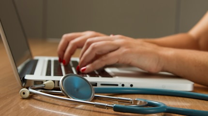 Healthcare professional using a laptop with a stethoscope nearby